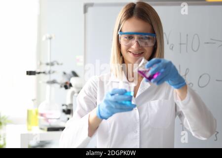 Woman scientist in safety glasses pouring chemical solution from flask in laboratory Stock Photo