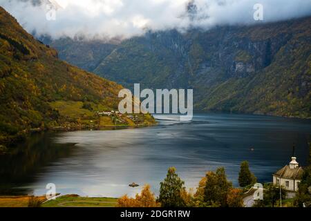 View over the Geiranger fjord in Norway on an autumns day with the local chapel in the frame and low cloud cover among the mountains.  Stock Photo