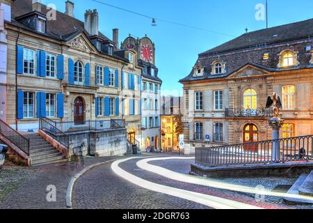 Evening scene along the Rue du Chateau climbing toward the castle in the old town of Neuchatel, Switzerland. A passing car around Fountain du Griffon Stock Photo