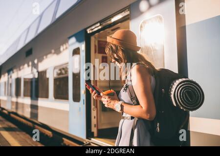 Railroad theme. Beautiful young woman with a backpack uses the phone while standing near the railroad train on the platform. Che