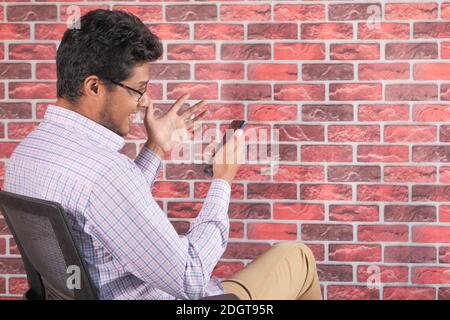 young man sitting on a chair In a video conference discussing on smart phone  Stock Photo