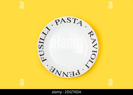 A deep white plate with pasta names on a yellow background Stock Photo