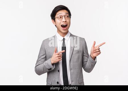 Waist-up portrait of excited, amazed and happy young emotive asian office manager, businessman in grey suit, seeing something aw Stock Photo