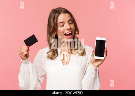 Finance, shopping and technology concept. Close-up portrait of excited good-looking blond girl in white dress, renew her spring Stock Photo