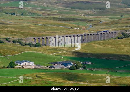 Scenic countryside view (Northern train crossing Ribblehead Viaduct, dramatic hilly uplands, sunlit valley) - Ribblesdale, Yorkshire Dales, England UK Stock Photo