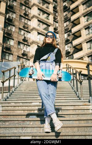 Urban woman with skate. Hipster girl with skateboard in city. Extreme sport and emotions concept. Alternative lifestyle. Stylish Stock Photo