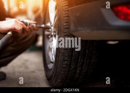 Auto mechanic man with electric screwdriver changing tire outside. Car service. Hands replace tires on wheels. Tire installation concept. Stock Photo