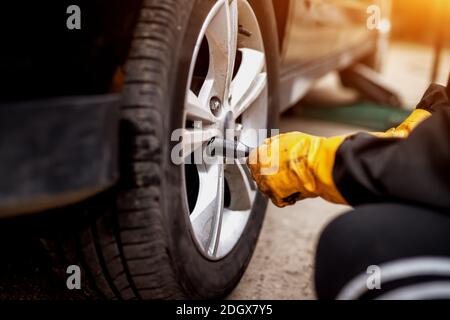An experienced hard working mechanic in orange gloves is using an electric wrench to tighten up the screws in a car wheel. Stock Photo