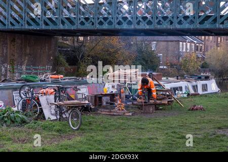 Resident houseboat owner sawing fire wood on the Lea Valley Navigable canal in Autumn Stock Photo
