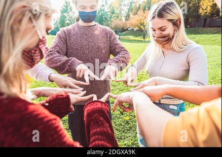 Group of young people standing on a circle with face mask doing symbol with fingers together at the park - New normal lifestyle concept of friends wit Stock Photo