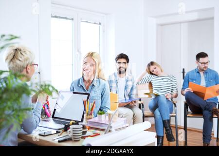 Beautiful young confident girl is having a job interview while others are waiting patiently. Stock Photo