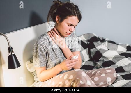 The theme is seasonal cold, runny nose flu virus infection. Young caucasian woman at home bedroom bed uses spray drops of medici Stock Photo