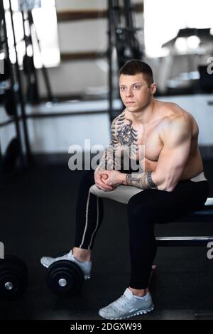 young bodybuilder sitting on a bench in the gym. Stock Photo