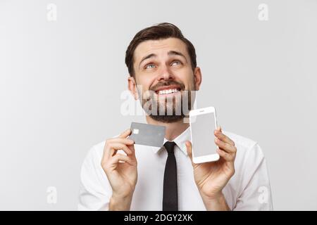 Photo of confident entrepreneur man in suit and tie holding smartphone and credit card for paying online isolated over gray back Stock Photo