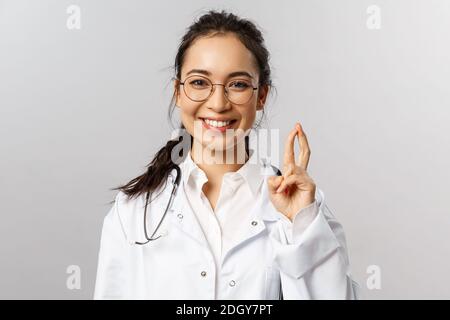 Close-up portrait of enthusiastic, smiling attractive asian female doctor, therapist check-up child in hospital, showing few tri Stock Photo