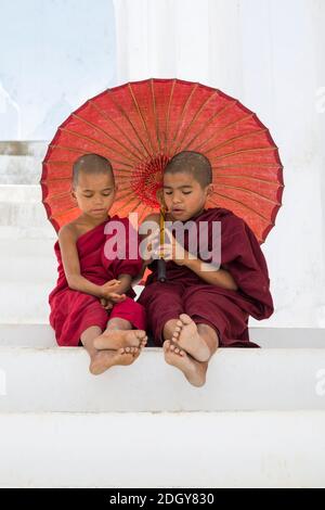 Young novice Buddhist monks holding parasols at Myatheindan Pagoda (also known as Hsinbyume Pagoda), Mingun, Myanmar (Burma), Asia in February Stock Photo