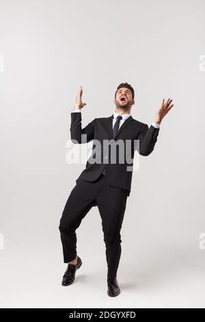 Cheerful young bearded business man show hand up excited with clenched fists. Full length portrait business man isolated over wh Stock Photo