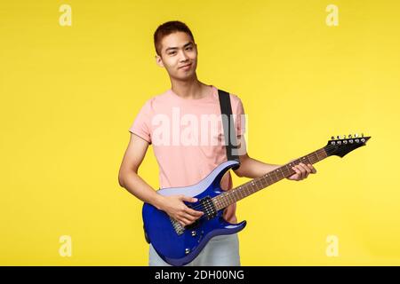 Lifestyle, leisure and youth concept. Portrait of smiling asian young man playing in band, holding electric guitar, practicing m Stock Photo