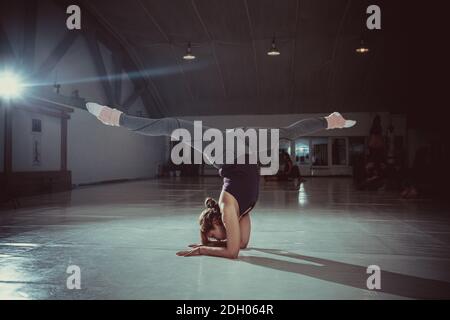 Young attractive yogi woman practicing yoga concept, standing in variation of Pincha Mayurasana exercise, handstand pose, workin