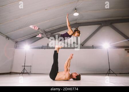 Young couple Couple practicing acro yoga in gym. Healthy lifestyle. Acroyoga. Couple yoga. Partner yoga. Muscular man throwing w Stock Photo