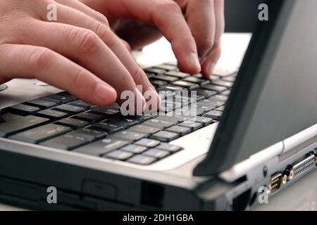 A closeup of a man's hands as he types on his laptop computer keyboard at work in an office or on the go. The computer is old and outdated. Stock Photo