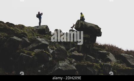 People posing for a photograph outdoors with a dog ignoring instructions in the countryside, Pancake Stone, Ilkley Moor, West Yorkshire, England, UK Stock Photo