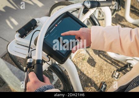 Girl renting city bike from bike stand in Copenhagen, Denmark February 18, 2019. Beautiful woman taking bicycle for rent. Happy Stock Photo