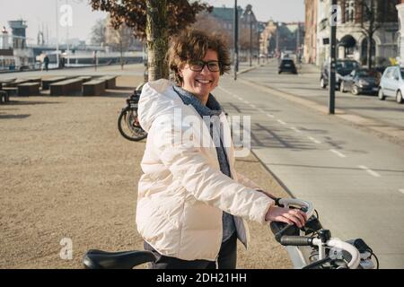 Happy woman renting bicycle at public urban cycle transport station in Copenhagen, Denmark. Young woman taking a shared bicycle. Stock Photo
