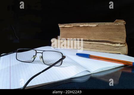 The Spectacles,note pad and handle to rest upon glass table. The Subjects for learning on black background. The Old books. Stock Photo