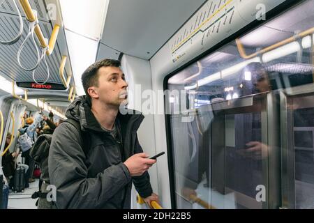 Caucasian male tourist with a backpack in the subway Copenhagen, Denmark. Passenger with smartphone looking at information board Stock Photo