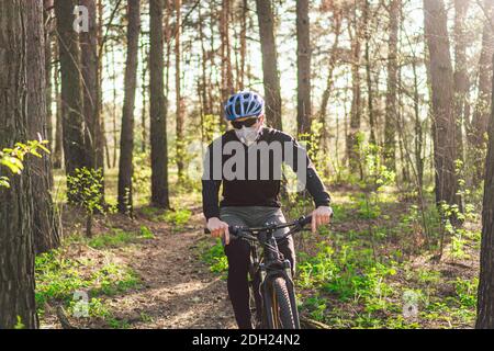 Cyclist wearing pollution mask. Young guy in respirator with filter pm 2.5 with ride on bike in park. Covid 19 Quarantine Sport. Stock Photo