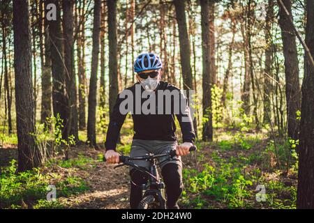 Cyclist wearing pollution mask. Young guy in respirator with filter pm 2.5 with ride on bike in park. Covid 19 Quarantine Sport. Stock Photo