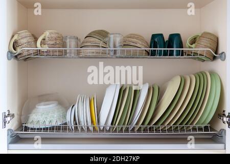 Clean dishes in white and green tones in a drying cabinet. Cups, glasses, mugs, plates, bowls, saucers on metal shelves. Concept for kitchen interior, Stock Photo