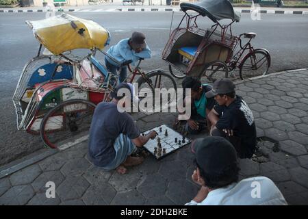 Drivers play chess sitting on the pavement next to their cycle rickshaws known locally as the becaks in Alun Alun Utara square in Yogyakarta in Central Java, Indonesia. Stock Photo