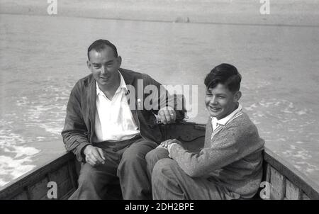 1950s, historical, out at sea, a father steering the small outboard motor on a wooden boat with his son on a fishing trip, Deal in Kent, England, UK. Stock Photo