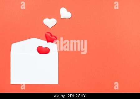 Opened white envelope and many hearts on a red background with copy space. Stock Photo