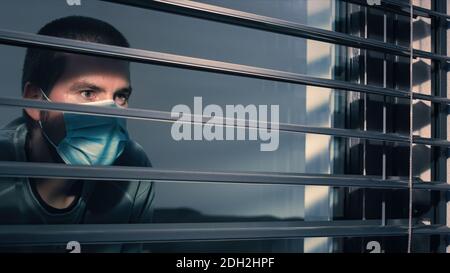 Coronavirus lockdown. Man with face mask looking through window. Stock Photo