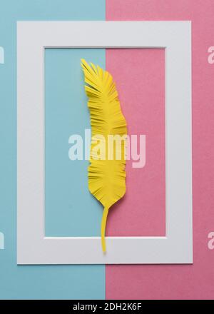 white frame with yellow paper feather  on colorful pink and blue background vertical composition Stock Photo
