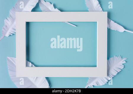 white frame with white paper feathers on blue background with copy space Stock Photo