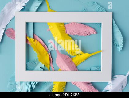 white frame with colorful paper feathers on blue background Stock Photo