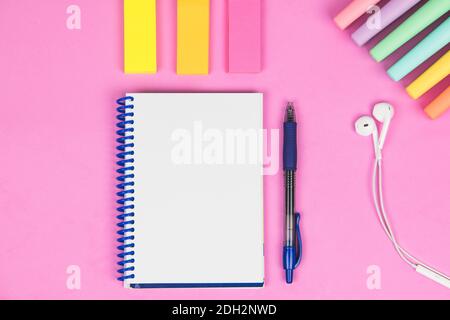blank notebook on a pink background with pen, colored post, headphones and colored markers Stock Photo
