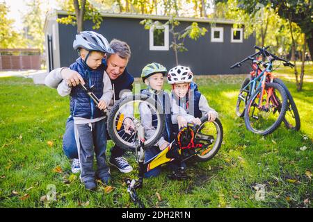 Father's day A big friendly family father and three sons joint active rest outside. Dad teaches sons to repair cycling. The chil