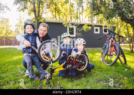 Father's day A big friendly family father and three sons joint active rest outside. Dad teaches sons to repair cycling. The chil