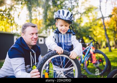 Father's day Caucasian dad and 5 year old son in the backyard near the house on the green grass on the lawn repairing a bicycle, Stock Photo