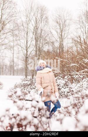 A young girl sits on a bench in a snowy park. It snows in winter. Girl in winter clothes in a snowy forest Stock Photo