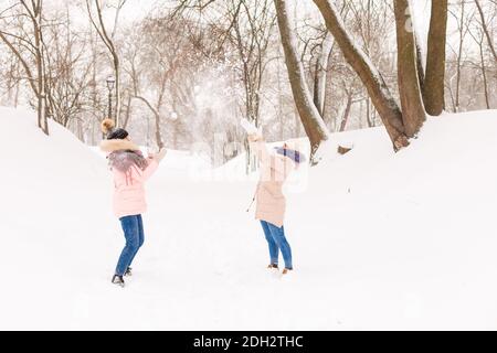 Two girls play snowballs in the winter in the forest. Sisters in a warm dress have fun with snow in winter Stock Photo