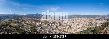 Aerial panorama of  Sangolqui in the Inter-Andean valley near Quito, Ecuador. With the Choclo (corn on the cob) roundabout in foreground and Cotopaxi Stock Photo