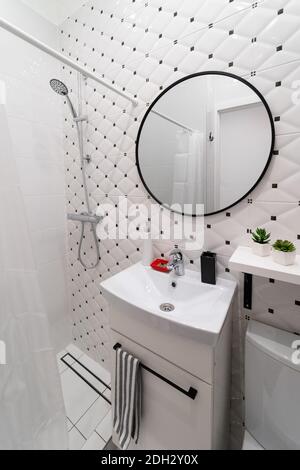 Part of a small modern stylish white black bathroom in the attic of an old house apartment with a sink on the cabinet and a round mirror Stock Photo