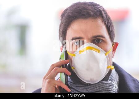 Flue and corona safety concept. Business man wearing face mask to protect himself and using smartphone. Outdoors Stock Photo