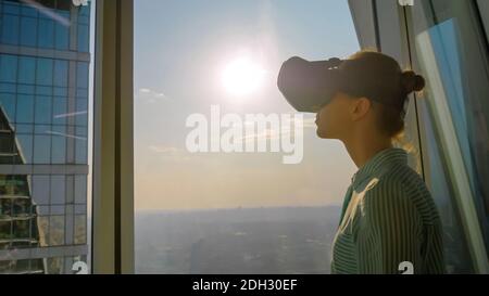 Young woman using virtual reality headset against skyscraper window - VR concept Stock Photo